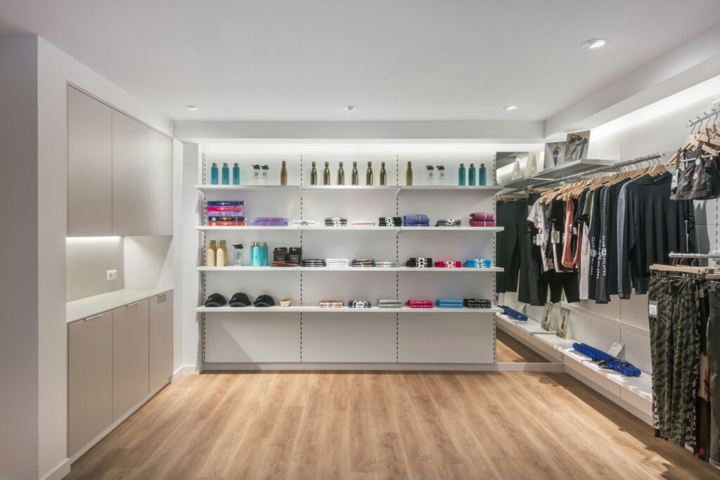 Espacio Comercial Minimalista Moderno con Ropa y Accesorios Organizados Tienda minorista brillante y espaciosa con diseño minimalista, que presenta paredes blancas, pisos de madera y ropa organizadamente dispuesta en percheros junto a estantes que exhiben varios productos.