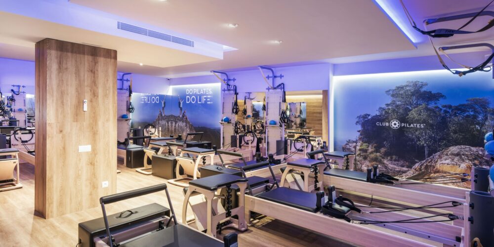 Vista interior de un estudio de Pilates de alta gama en Barcelona, con diseño moderno, máquinas de reformador de madera, iluminación natural y un mural inspirado en la naturaleza.