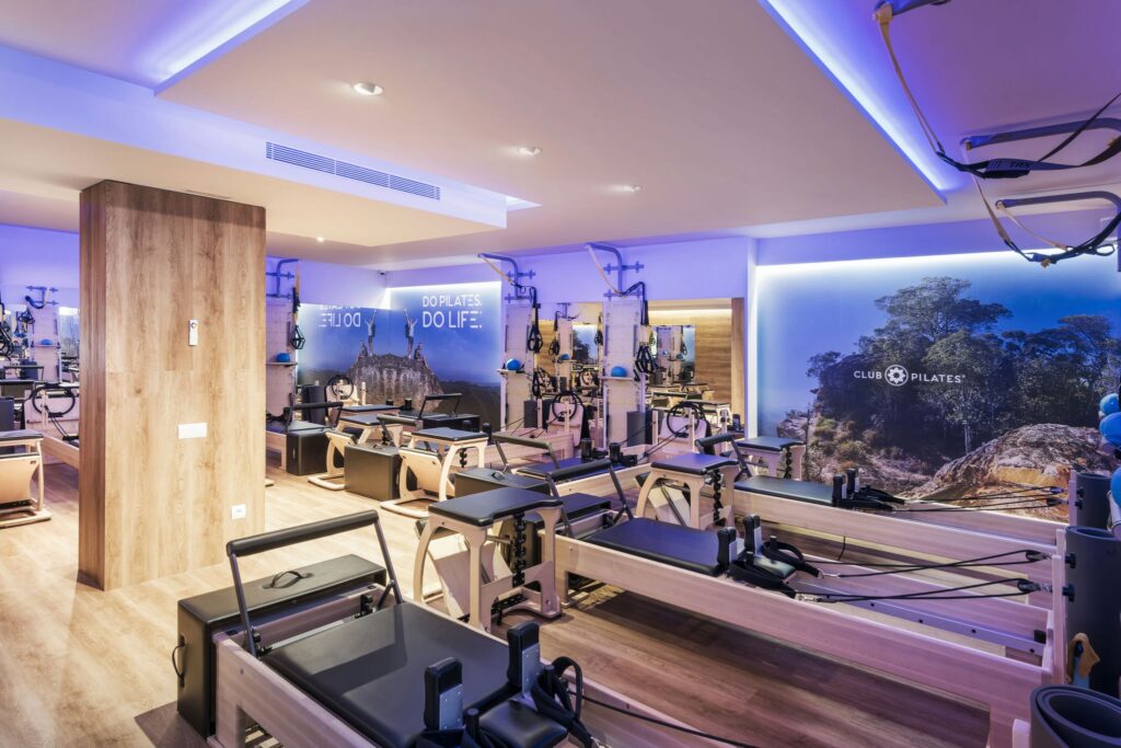 Estudio de Pilates de Alto Diseño en Barcelona con Elementos Contemporáneos Vista interior de un estudio de Pilates de alta gama en Barcelona, con diseño moderno, máquinas de reformador de madera, iluminación natural y un mural inspirado en la naturaleza.