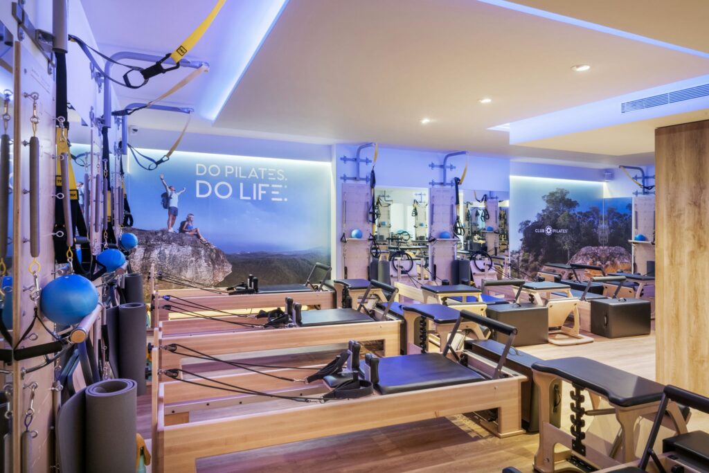 Estudio de Pilates Moderno en Barcelona: Diseño de Alta Gama Vista interior de un estudio de Pilates moderno en Barcelona, con suelos de madera, equipo de Pilates de calidad y una atmósfera contemporánea. Las paredes muestran imágenes motivacionales y la frase 'DO PILATES. DO LIFE.', destacando un entorno profesional e invitador para entusiastas del fitness.