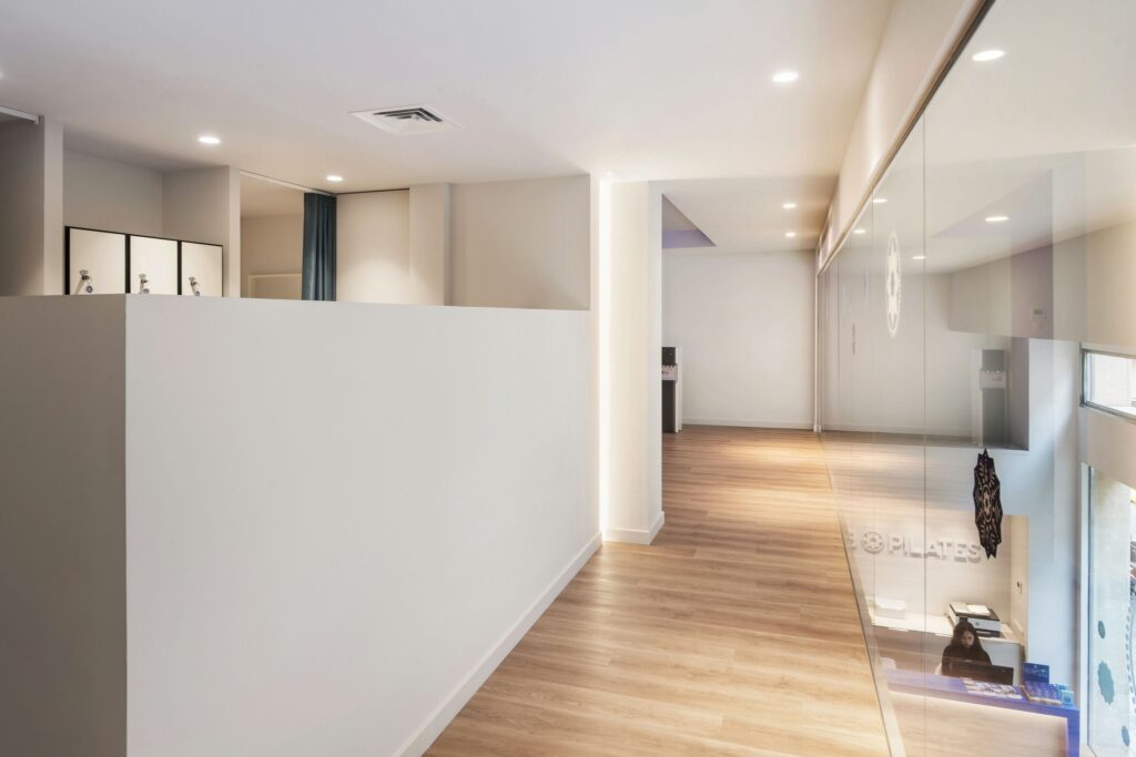 Diseño de interiores de alta gama en un moderno pasillo en Barcelona Moderno pasillo de diseño interior en Barcelona con suelos de madera pulida, paredes blancas y grandes paneles de cristal que permiten la entrada de luz natural.