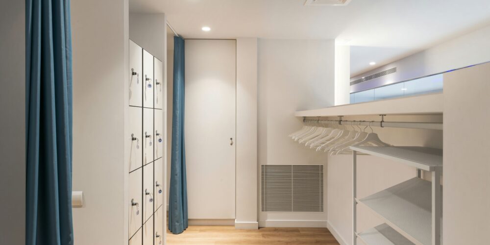 Espacio interior contemporáneo en Barcelona, con diseño minimalista, paleta de colores clara, lockers blancos, estantería montada en la pared, suelo de madera natural y cortinas azules suaves, resaltando la funcionalidad y estética de la arquitectura de alta gama.