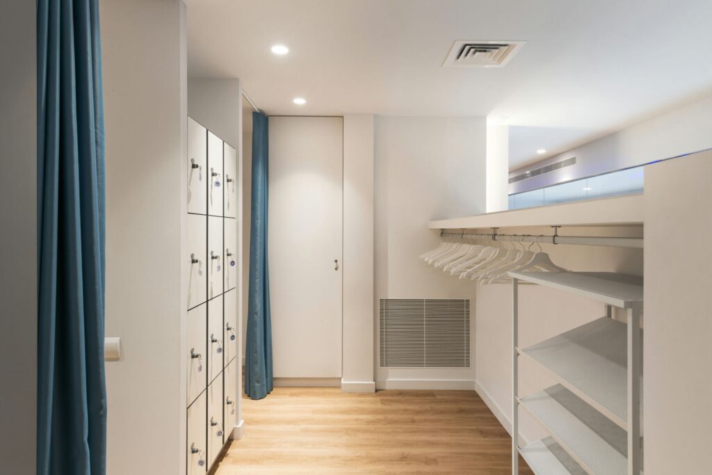 Vista del interior moderno y sofisticado en Barcelona con diseño minimalista Espacio interior contemporáneo en Barcelona, con diseño minimalista, paleta de colores clara, lockers blancos, estantería montada en la pared, suelo de madera natural y cortinas azules suaves, resaltando la funcionalidad y estética de la arquitectura de alta gama.