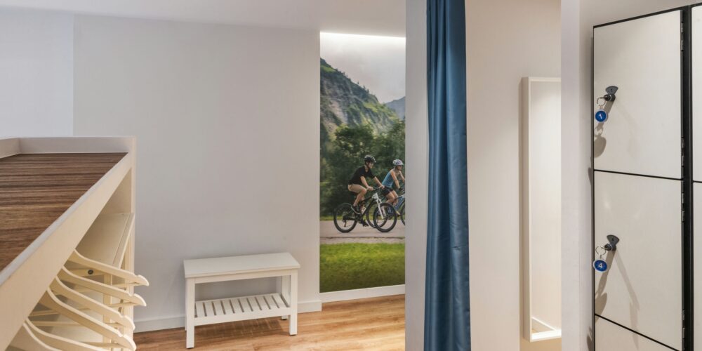 Diseño interior contemporáneo en Barcelona, mostrando un espacio funcional con suelos de madera, banco y sistema de taquillas, destacado por un mural de ciclistas.