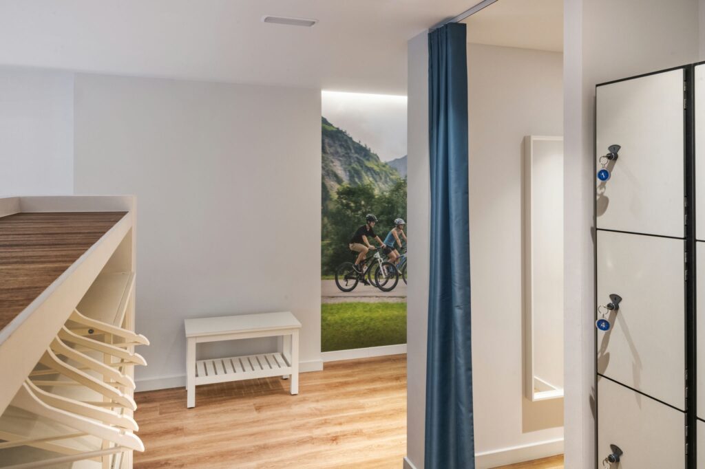 Proyecto de Diseño de Interiores Moderno en Barcelona con Murales Escénicos Diseño interior contemporáneo en Barcelona, mostrando un espacio funcional con suelos de madera, banco y sistema de taquillas, destacado por un mural de ciclistas.